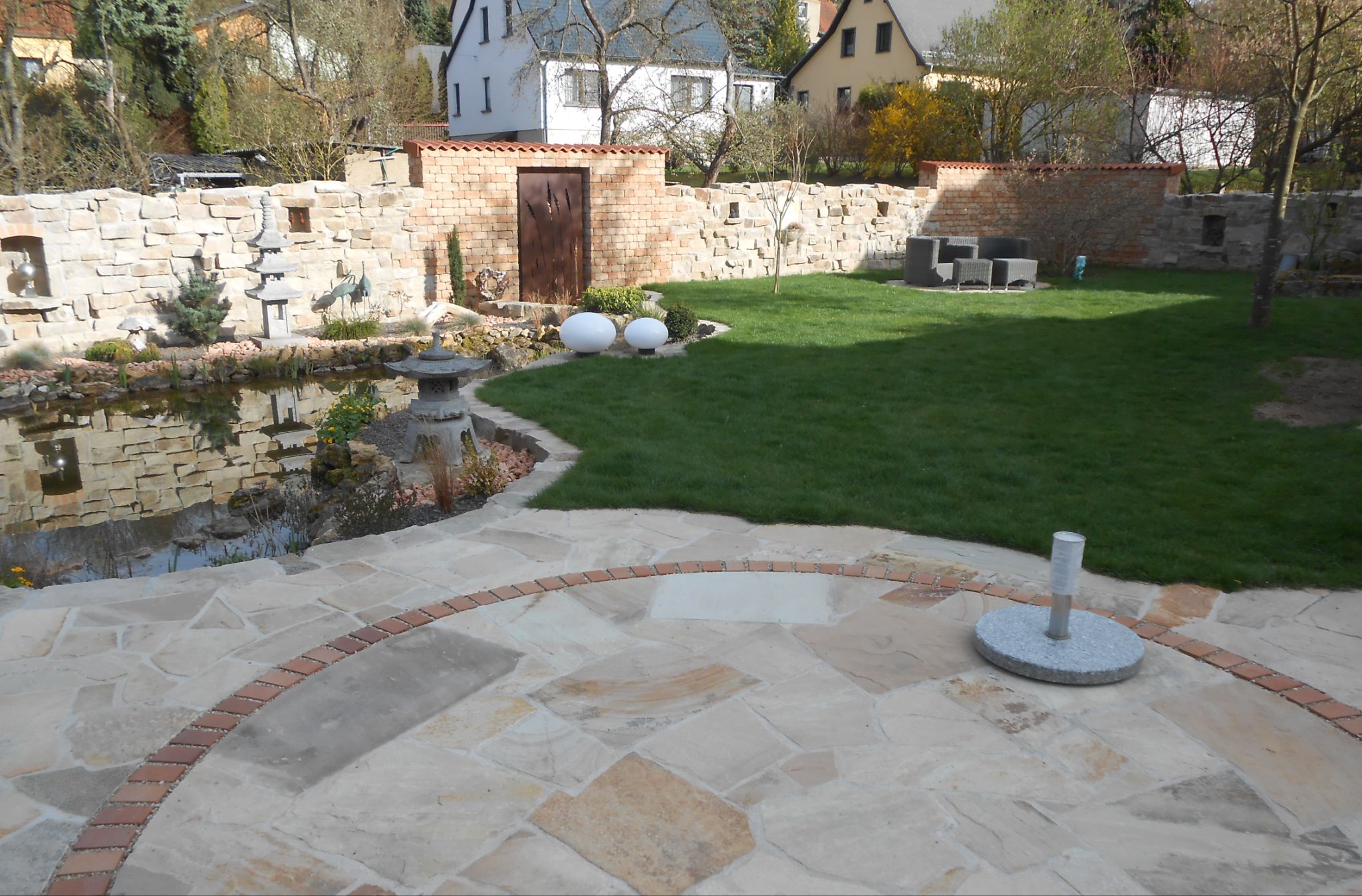 Natursteinmauern, Teich und Sandstein-Terrasse einer fertiggestellten Gartenanlage
